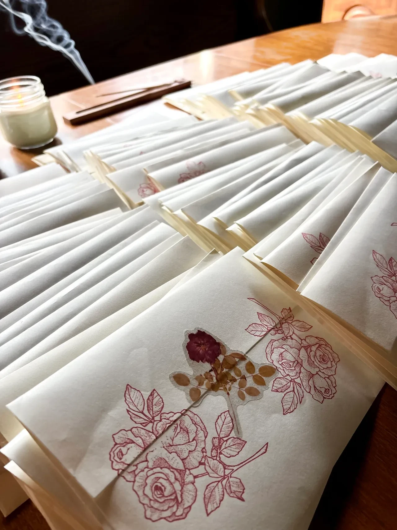 Hand holding a wax-sealed envelope with rose illustration against green grass