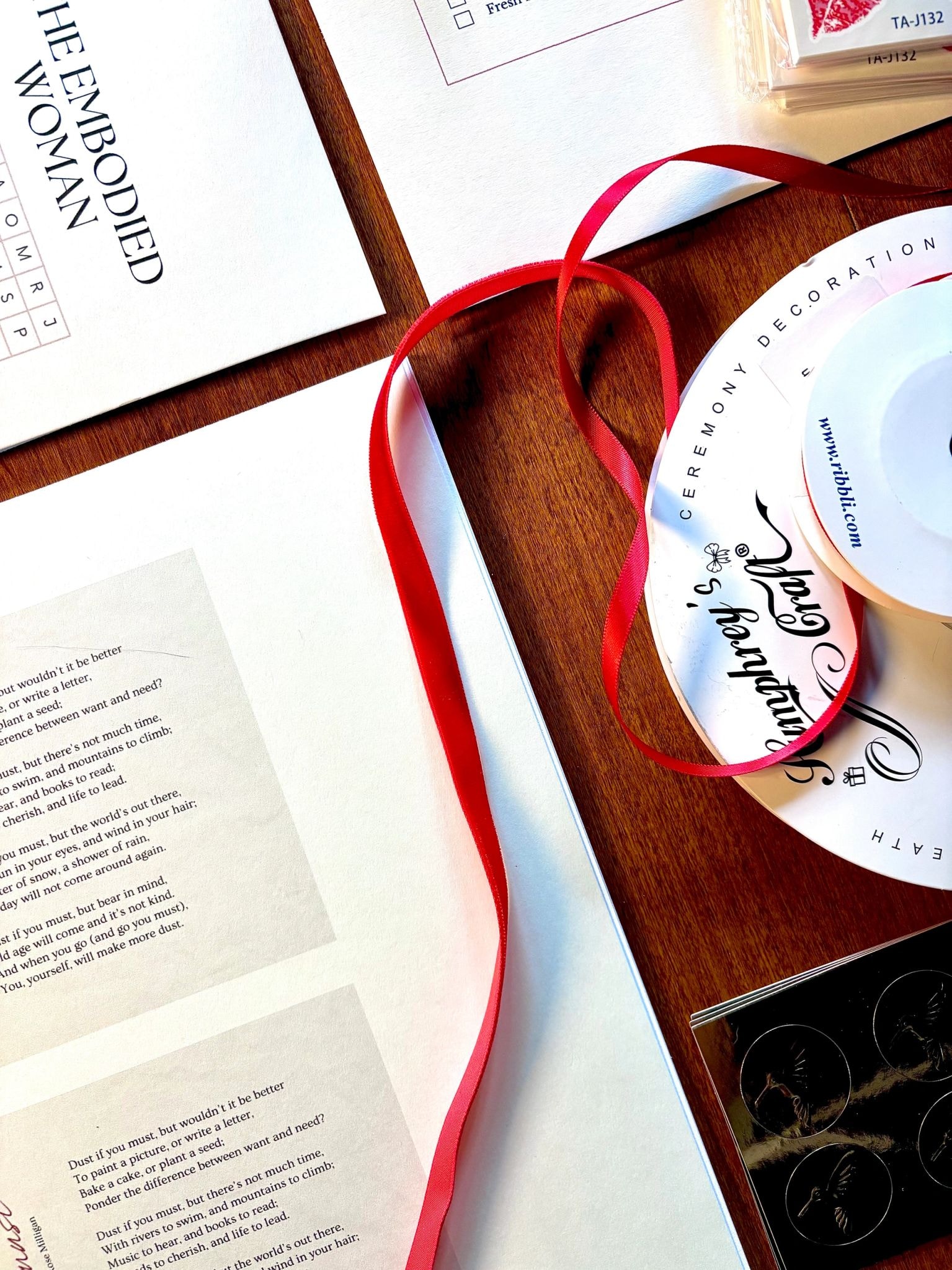 The Embodied Woman letter with red satin ribbon and ceremony decoration spool on wooden tray