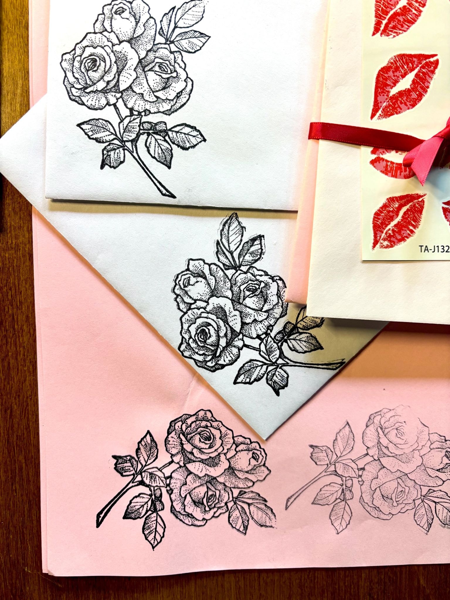 Rose illustrations stamped in black ink on layered pink and white envelopes with red lip prints